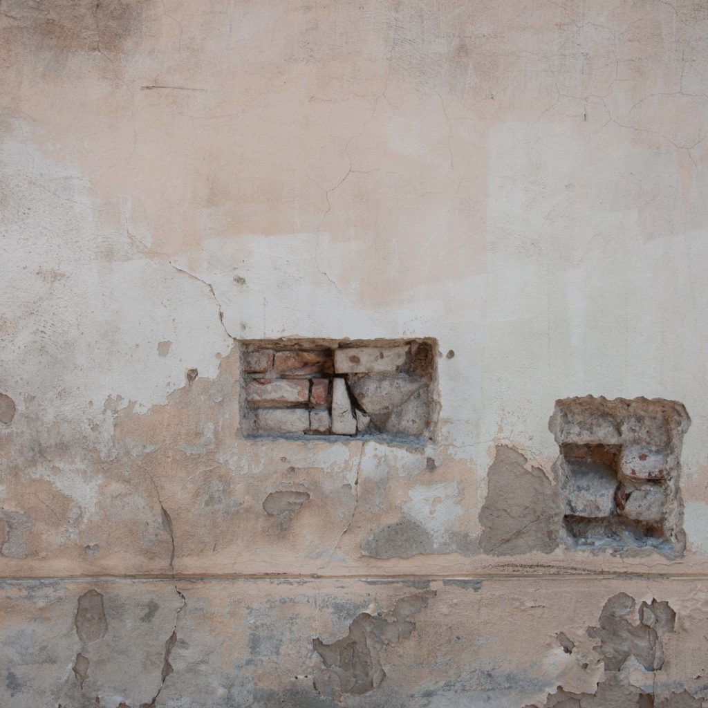 the artwork shows an old wall of a house with cracks and two rectangular holes